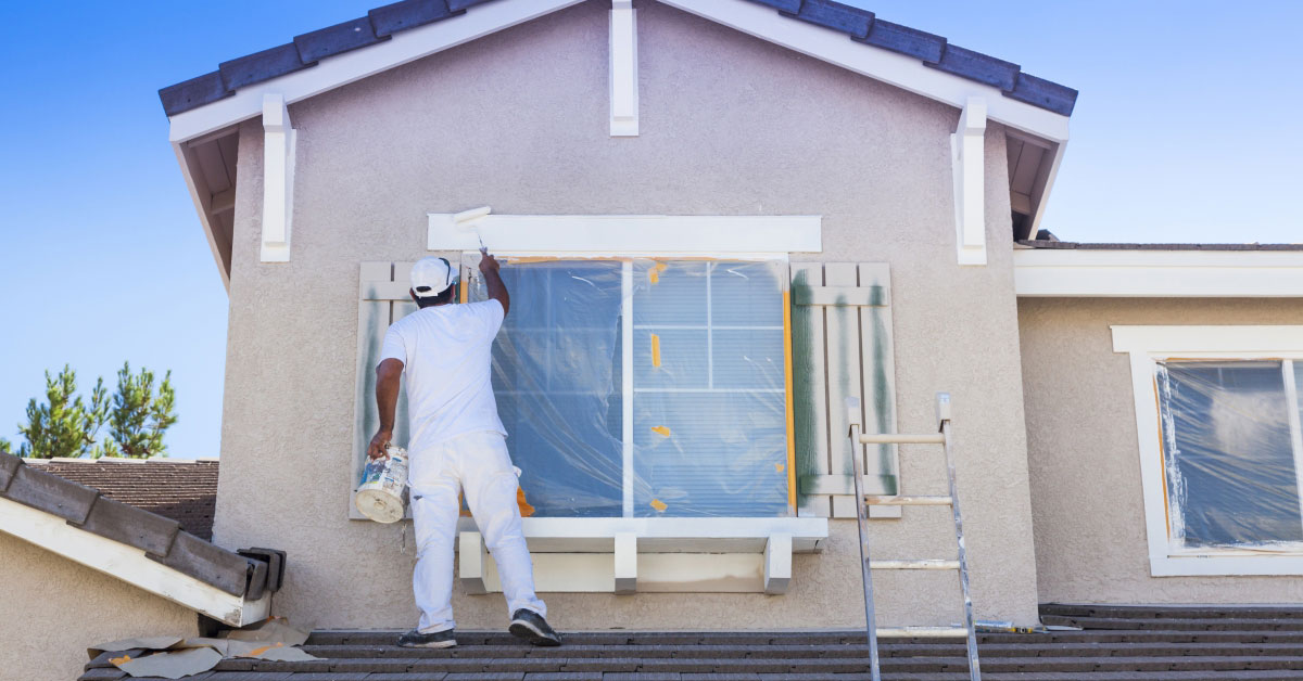 Workman painting the facade of a tan house