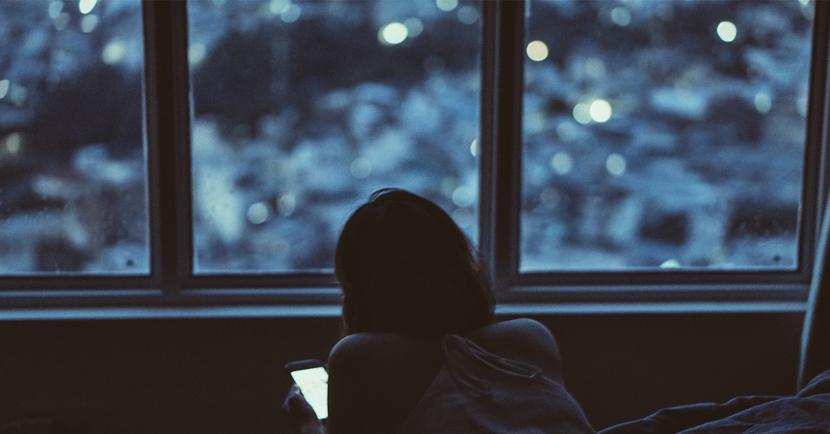 Woman on her phone sitting in front of a window in the dark