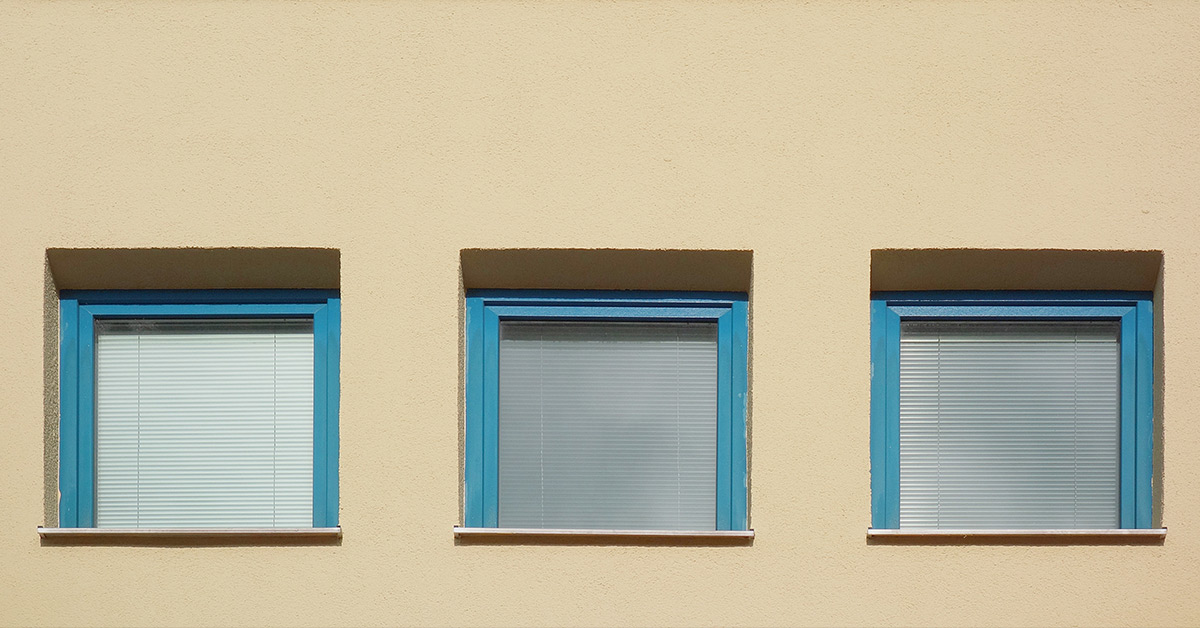 Three identical square windows on a tan wall with teal frames